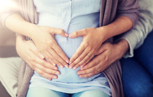 pregnant woman and husband making heart gesture with hand on belly 