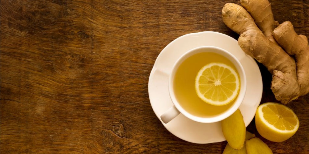 A cup of lemon ginger tea with half a lemon and ginger